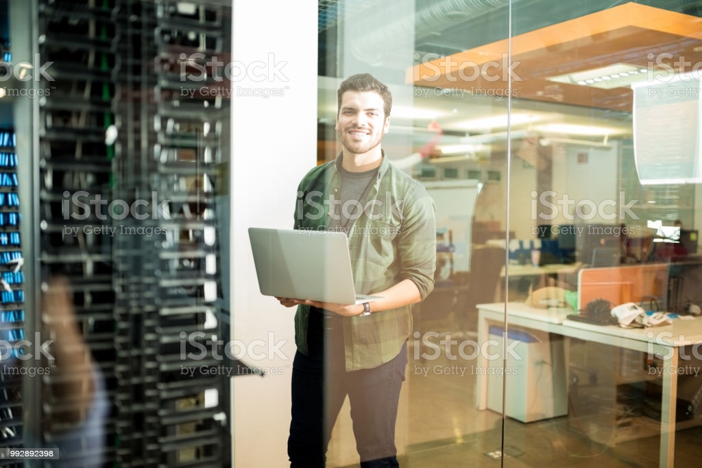 Portrait of happy male technician with laptop in large data center Portrait of happy male technician with laptop in large data center